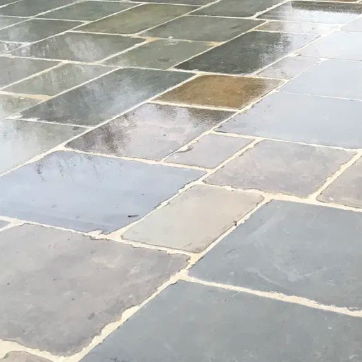 Natural slate flagstone pavers with irregular shapes and light gray mortar, shown wet with reflections on a patio surface.