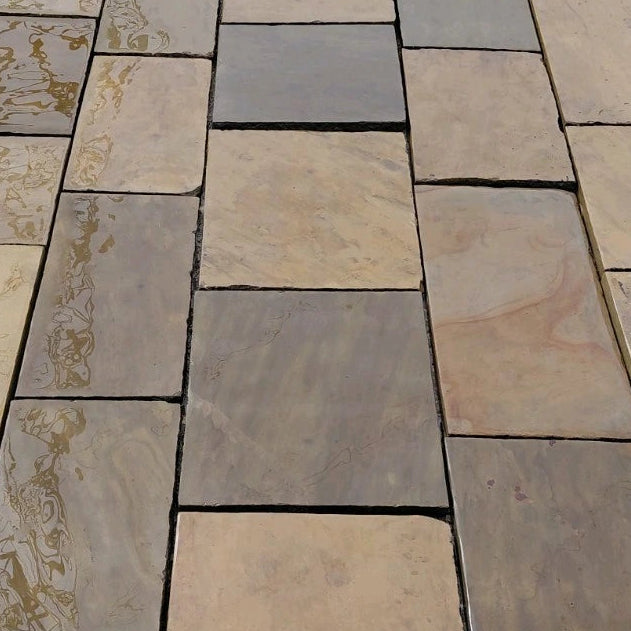 Natural stone paving tiles in a staggered layout, featuring a mix of warm beige, light brown, and cool gray stone surfaces with visible natural veining and texture.