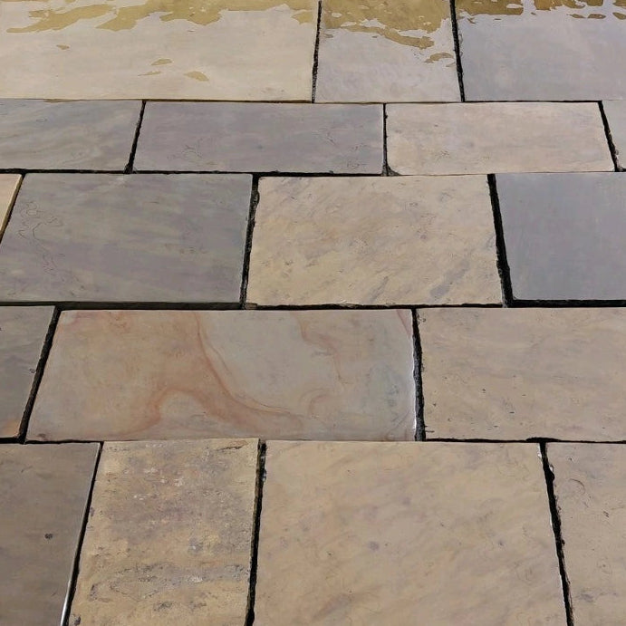 Natural stone pavers in a staggered layout, featuring a mix of warm beige, gray, and brown textured slabs with dark grout lines.